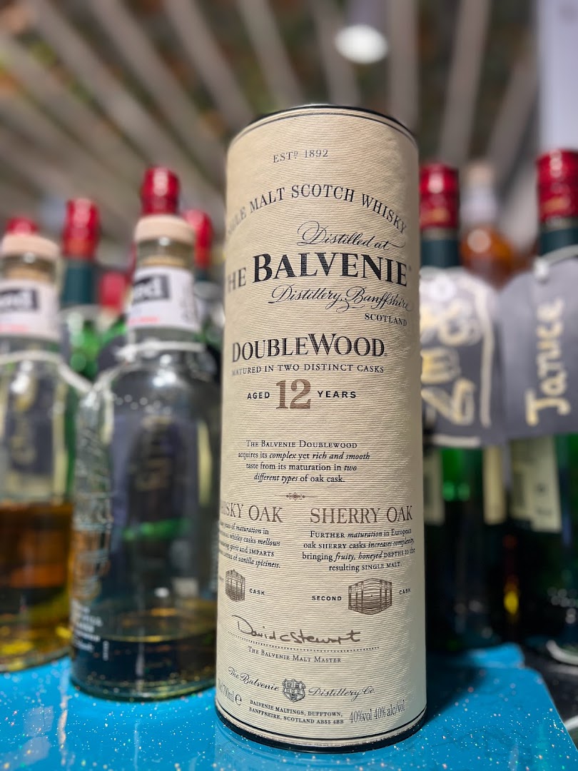 A close-up of a Balvenie DoubleWood 12 Years whisky packaging, surrounded by other bottles.