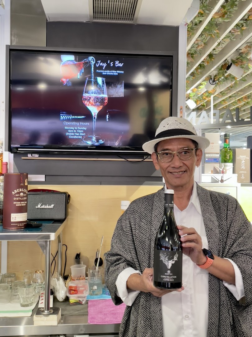 A man holds a wine bottle at Jay's Bar, with a screen displaying bar information and operating hours.