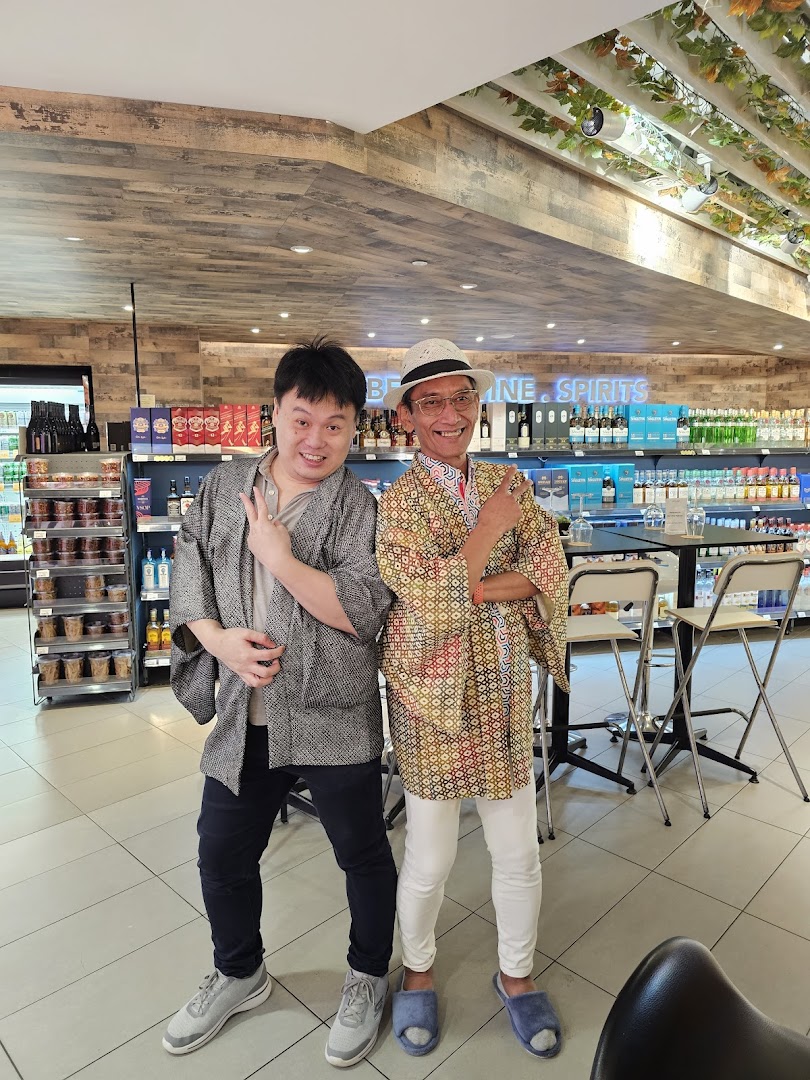 Two smiling individuals pose inside Jays Bar, surrounded by shelves of wine and spirits.