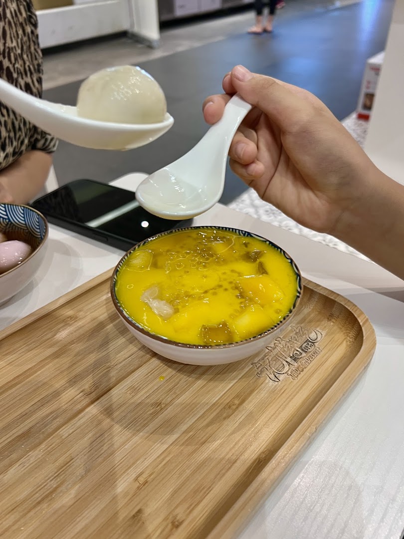 Close-up of hands enjoying vibrant mango dessert and glutinous rice balls on a wooden tray.