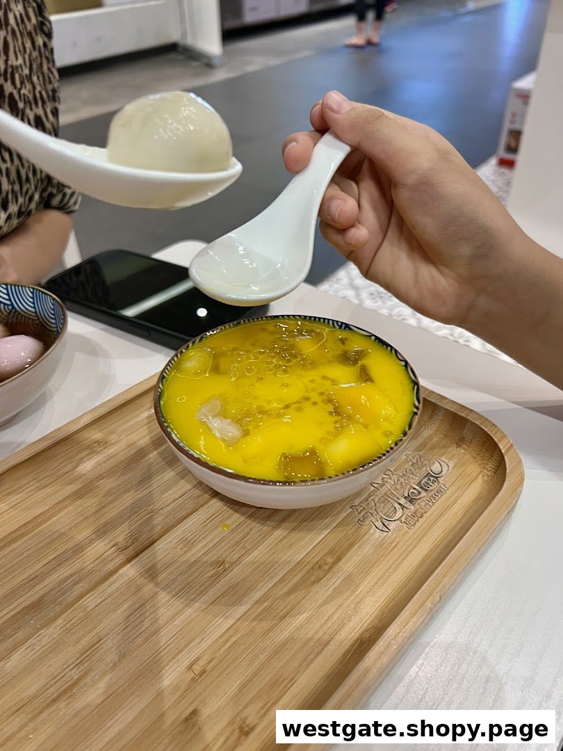 Close-up of hands enjoying vibrant mango dessert and glutinous rice balls on a wooden tray.