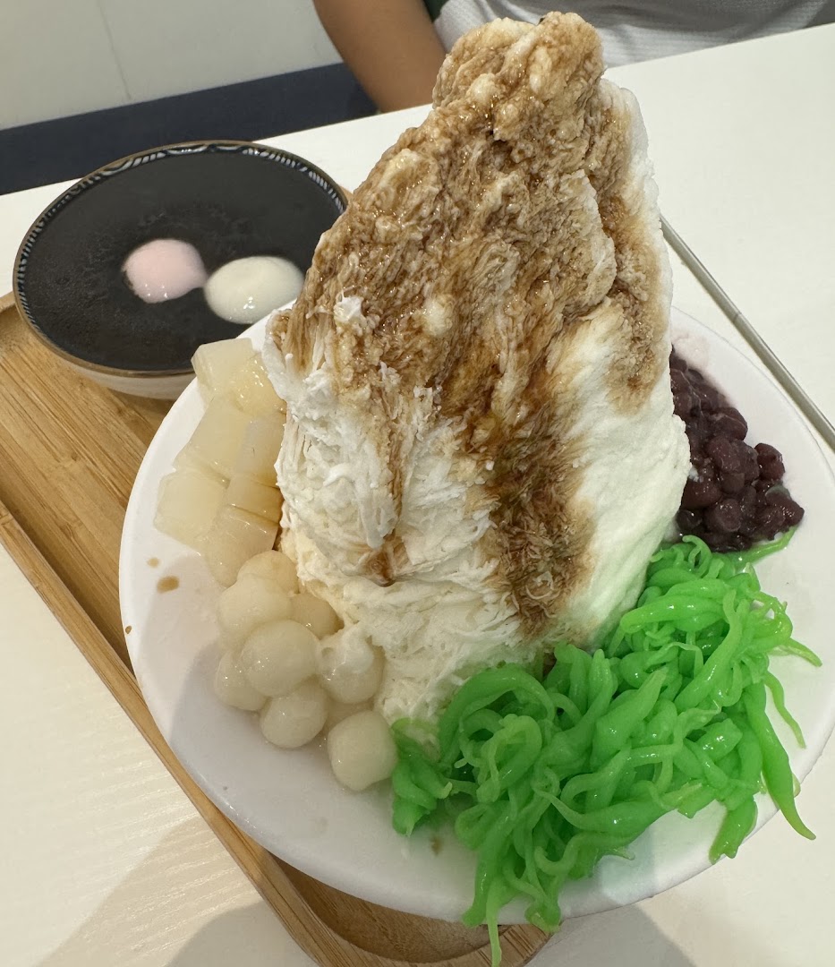 A large, refreshing shaved ice dessert with various toppings and a side of black sesame paste with mochi.
