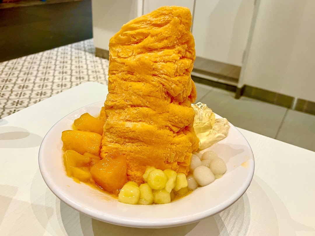 A vibrant mango shaved ice dessert with fresh mango chunks, mini mochi, and other toppings in a white bowl.