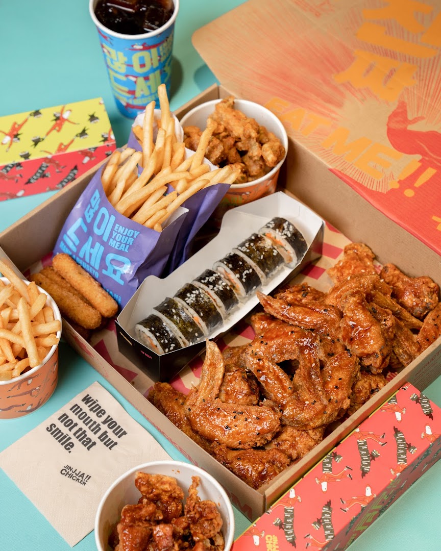 A delicious spread of JINJJA Chicken's Korean fried chicken, fries, kimbap, and sides in a takeout box.