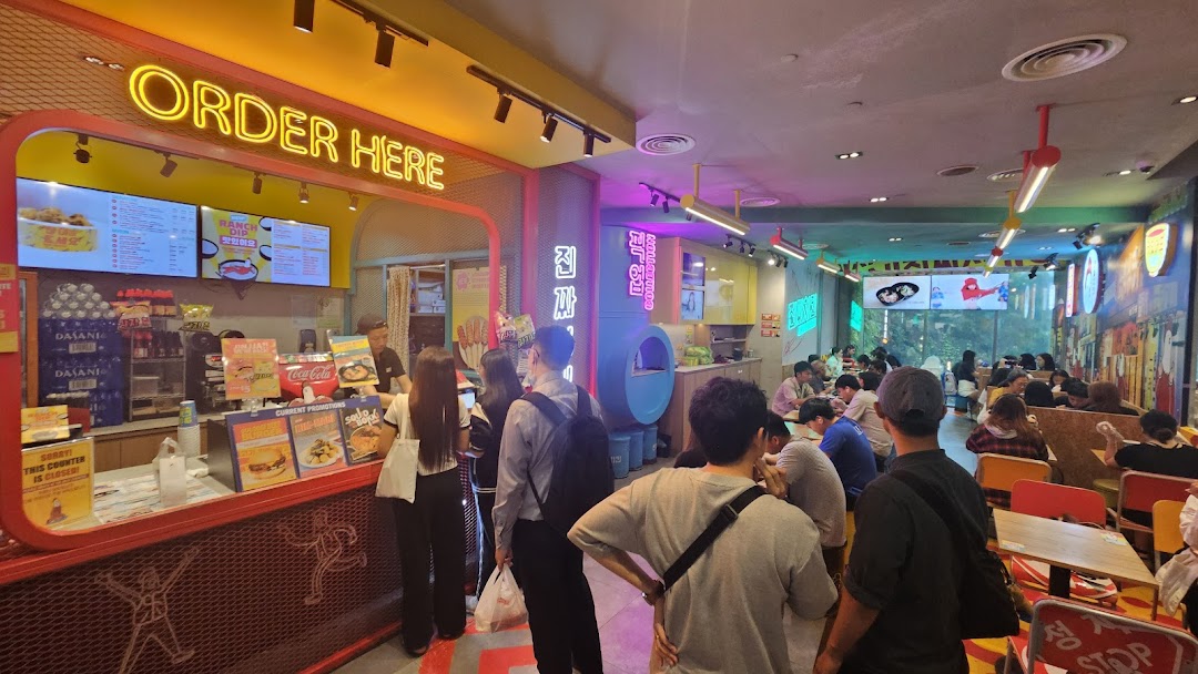 A vibrant interior shot of JINJJA Chicken, showing customers at the ordering counter and dining area.