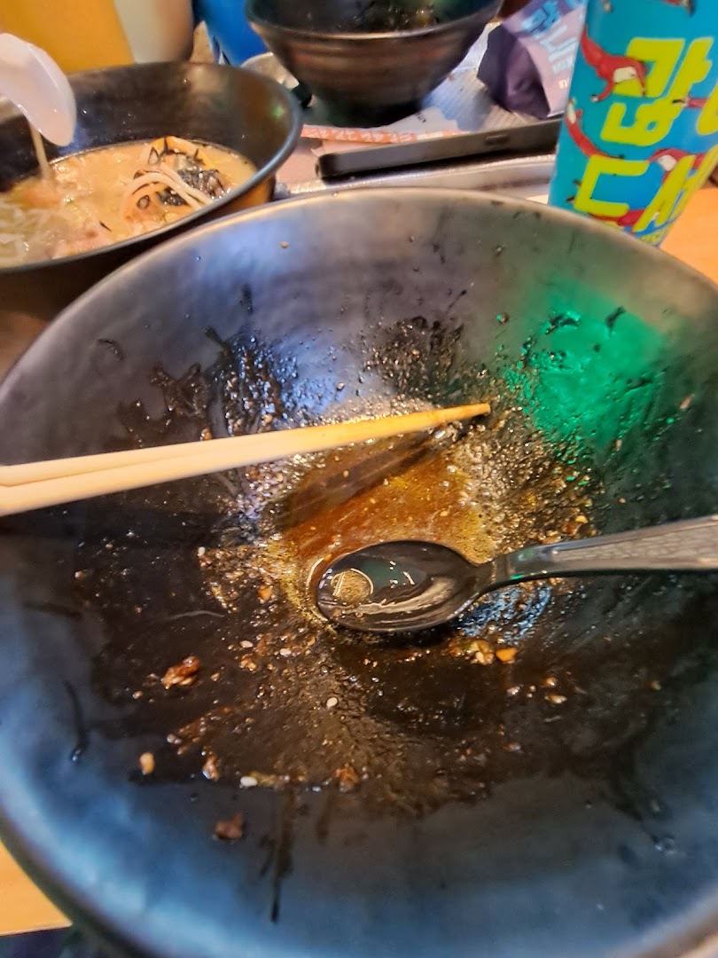 An empty ramen bowl with chopsticks and spoon, showing remnants of a delicious meal.