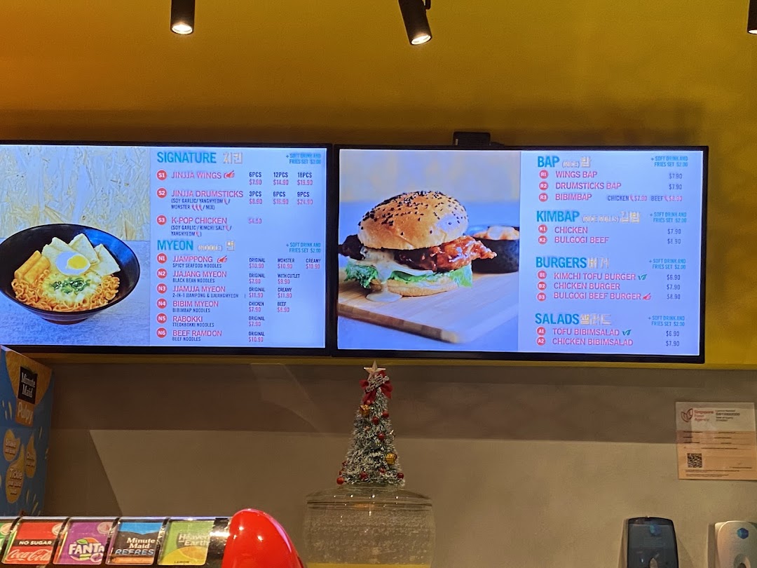 A digital menu board displaying various Korean dishes including chicken, noodles, rice, burgers, and salads.