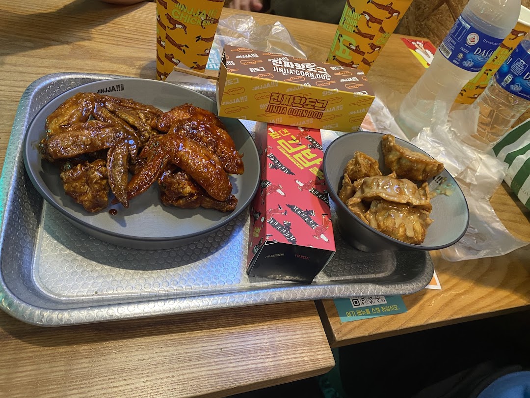A delicious spread of JINJJA Chicken's Korean fried chicken wings, dumplings, and a corn dog on a table.
