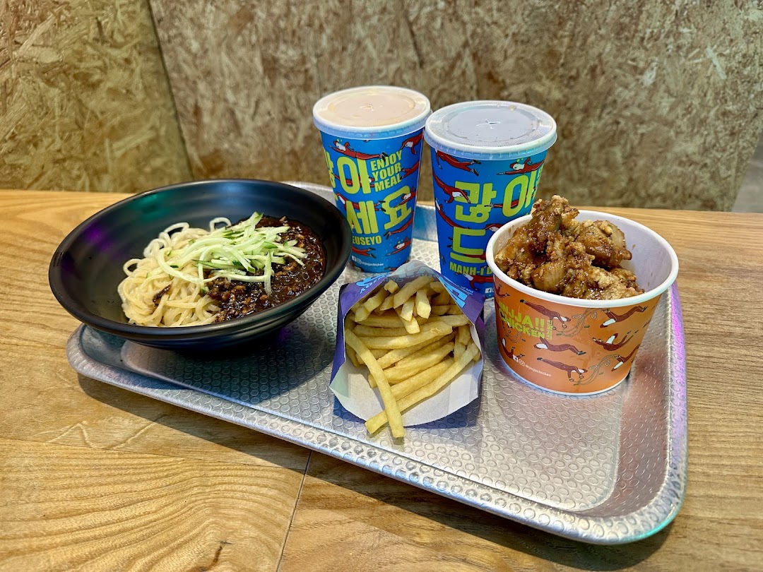 A tray with Korean black bean noodles, fried chicken, french fries, and two drinks.