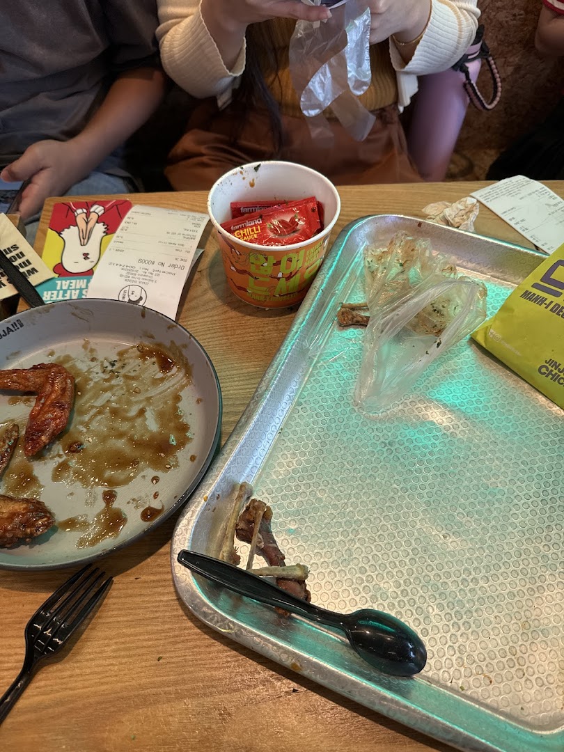 A table with leftover chicken wings, a receipt, and chili sauce packets after a meal.