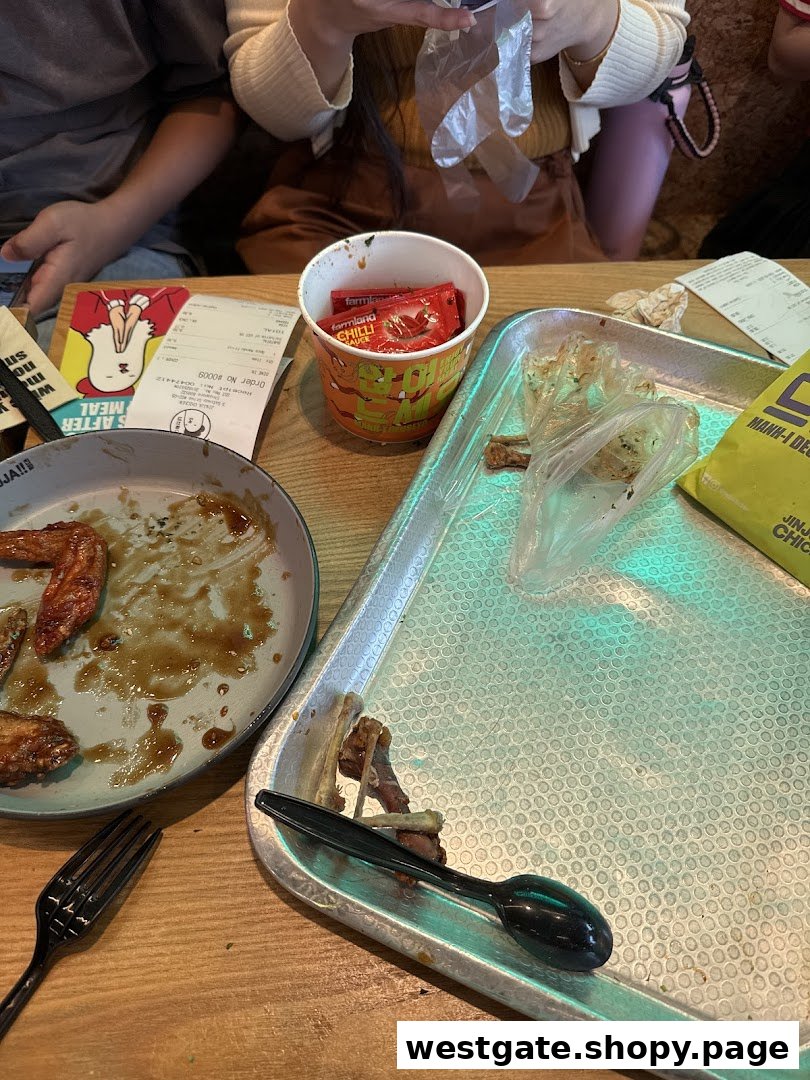 A table with leftover chicken wings, a receipt, and chili sauce packets after a meal.