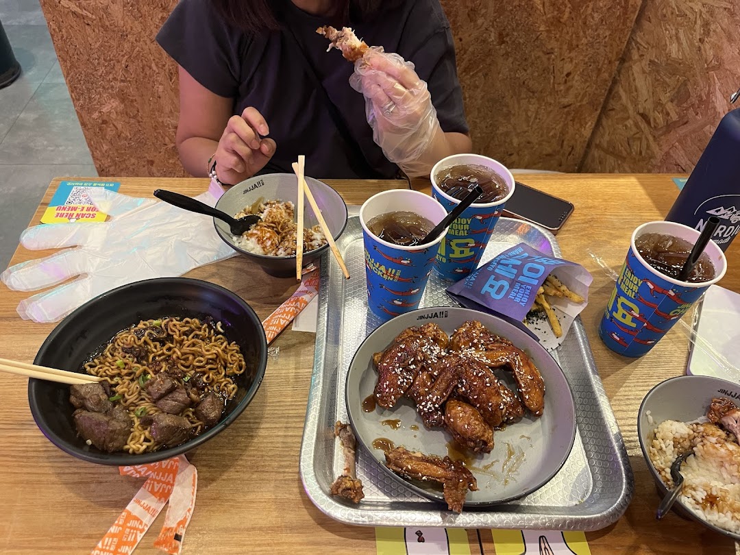 A table at JINJJA Chicken featuring Korean fried chicken, noodles, rice bowls, and drinks.