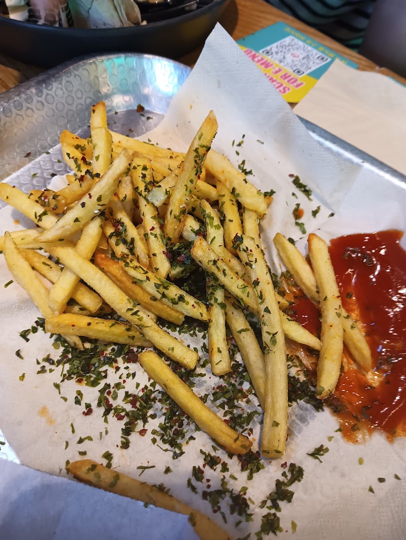 A close-up of golden french fries seasoned with herbs, served with a side of ketchup.