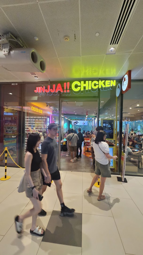 The vibrant storefront of JINJJA Chicken with neon signs and customers entering the restaurant.