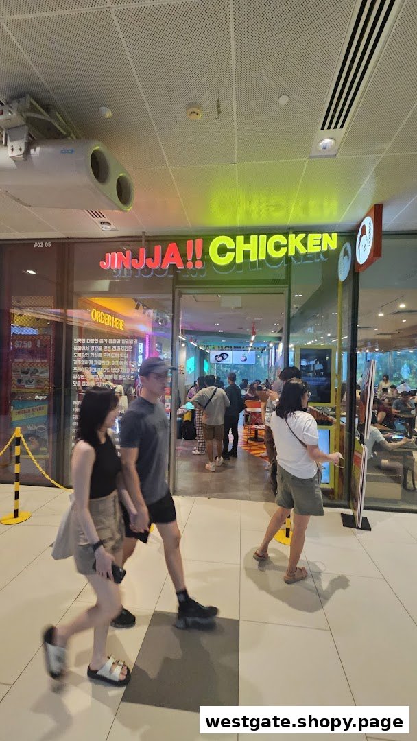 The vibrant storefront of JINJJA Chicken with neon signs and customers entering the restaurant.
