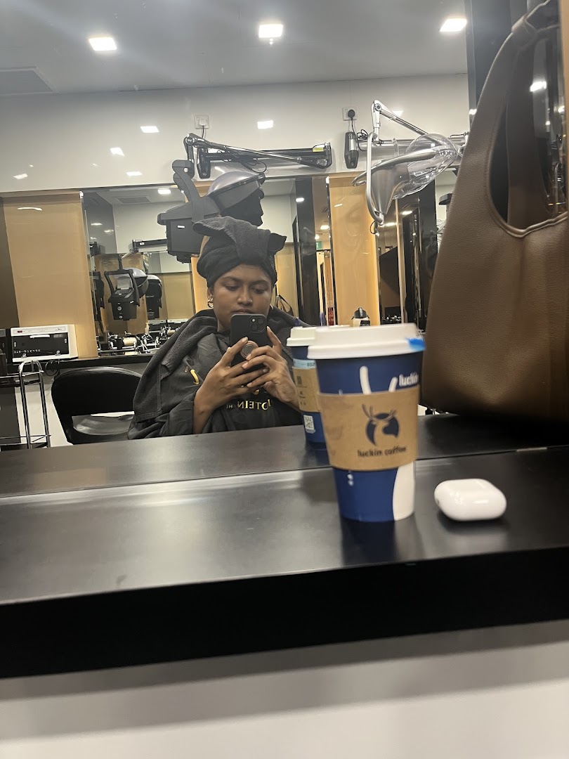 A person receiving a hair treatment, wrapped in a towel, using a phone, with a coffee cup nearby.