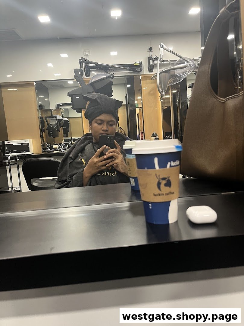 A person receiving a hair treatment, wrapped in a towel, using a phone, with a coffee cup nearby.