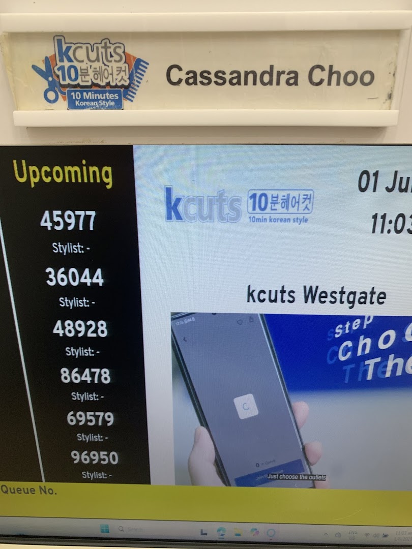 A digital queue display showing upcoming numbers and a staff name tag at kcuts.