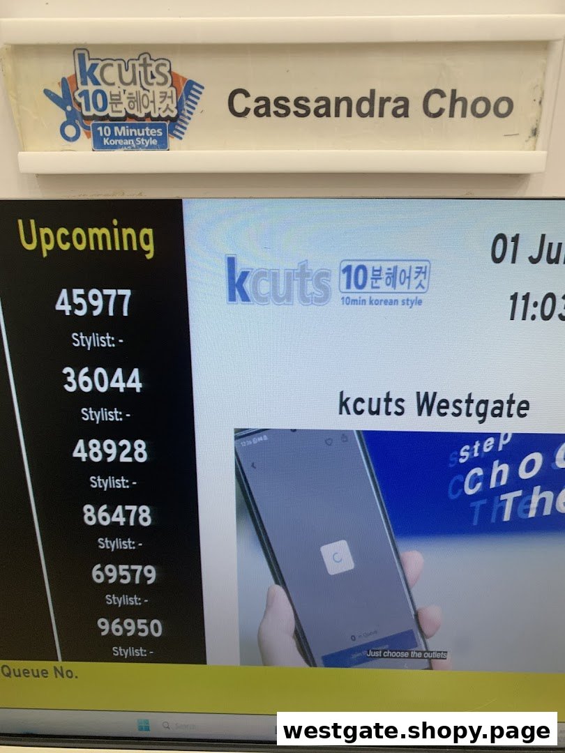 A digital queue display showing upcoming numbers and a staff name tag at kcuts.