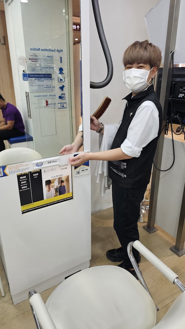 An kcuts employee smiles, holding a brush, next to a queue system in the salon.