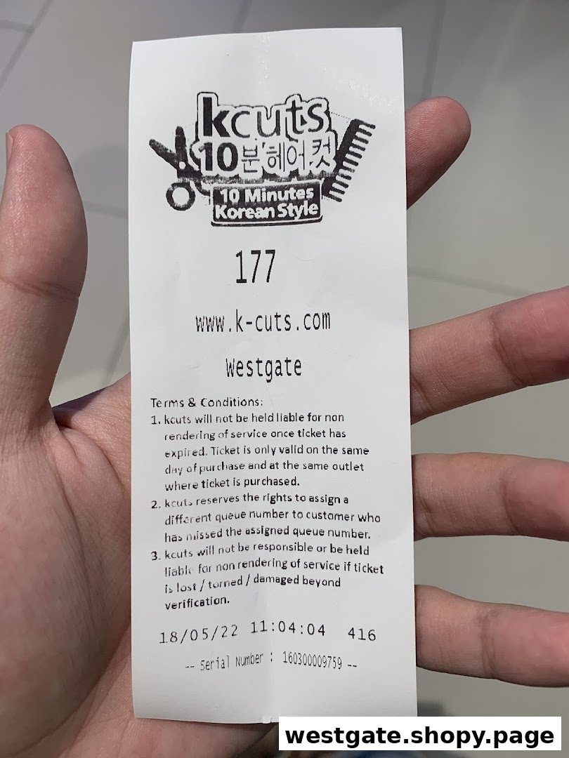 A hand holds a kcuts queue ticket from Westgate, detailing terms and conditions.