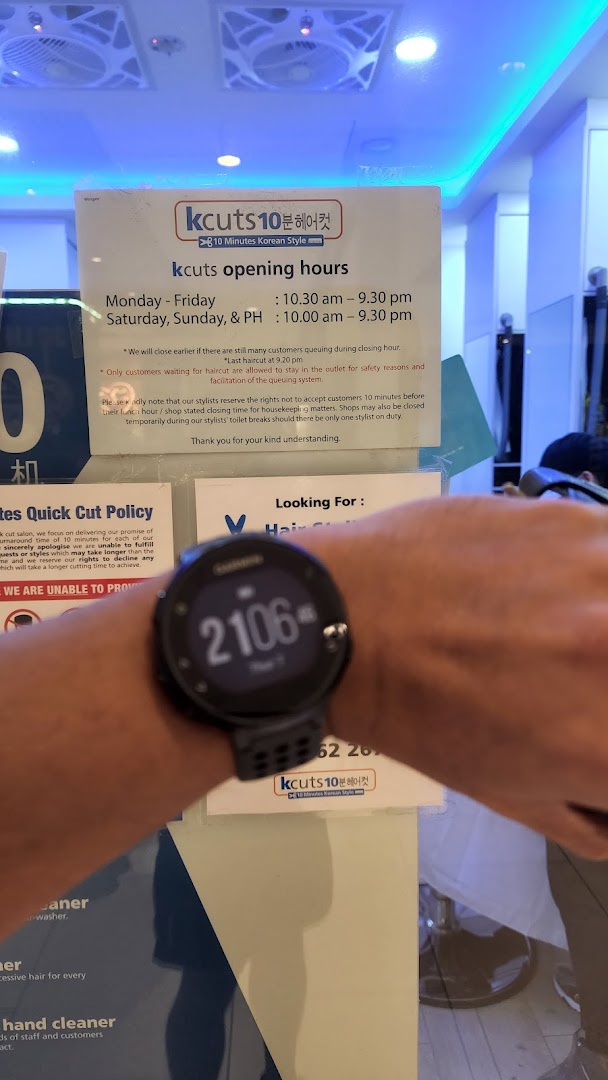 A person's arm with a smartwatch in front of kcuts opening hours and policy signs.