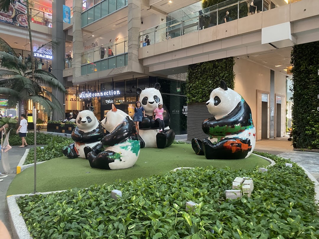 Four colorful panda statues in a green outdoor mall area with children playing.