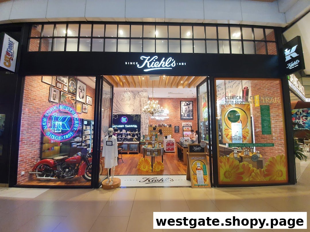 The storefront of Kiehl's Westgate, featuring a vintage motorcycle, neon sign, and product displays.