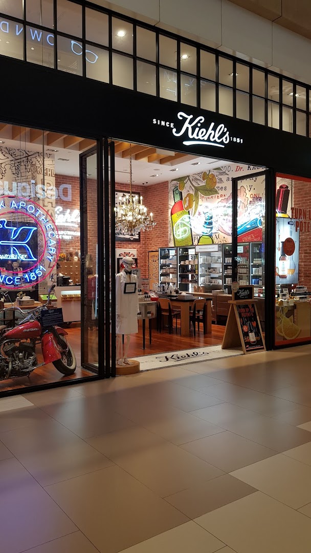 The storefront of Kiehl's, featuring a vintage motorcycle, neon sign, and a view into its apothecary-style interior.
