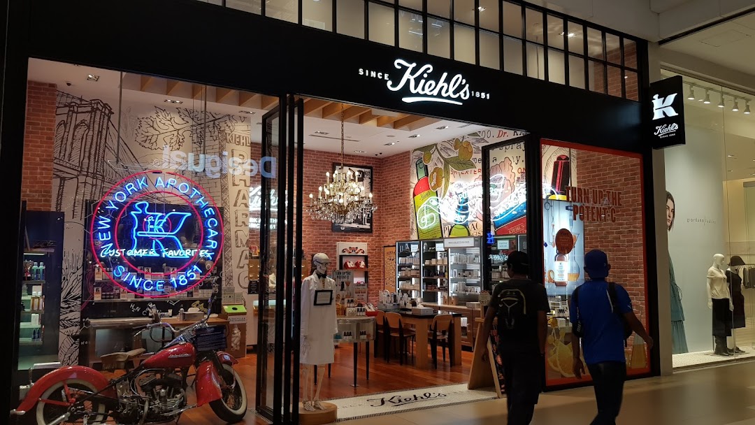 The storefront of Kiehl's, featuring a vintage motorcycle, neon sign, and a glimpse into its unique apothecary-style interior.