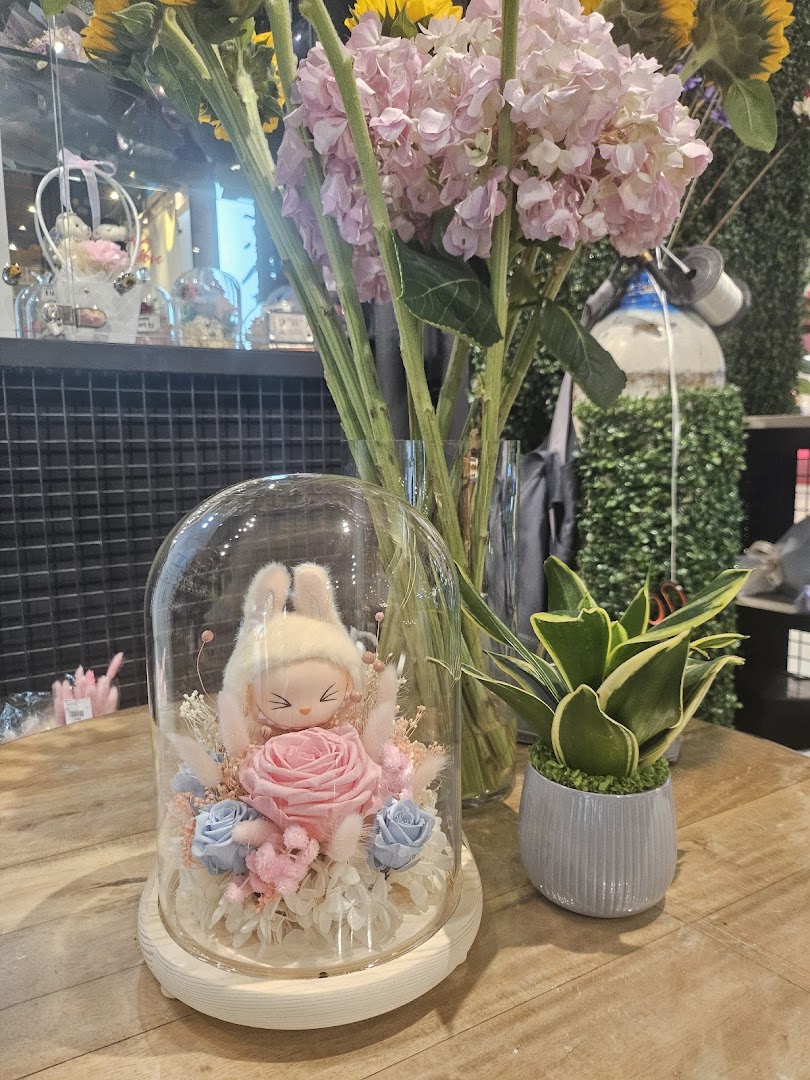 A charming floral arrangement with a plush toy under a glass dome, alongside a potted plant.