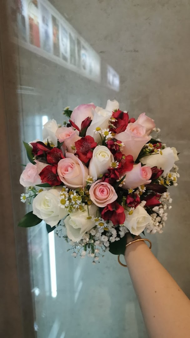 A hand holds a vibrant bouquet of pink, white, and red roses with delicate filler flowers.