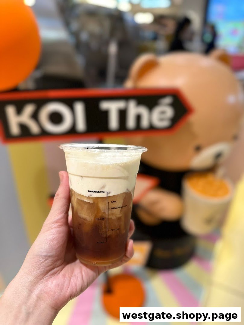 Hand holding a KOI Thé cream foam tea, with tea origins marked on the cup, in front of a shop display.