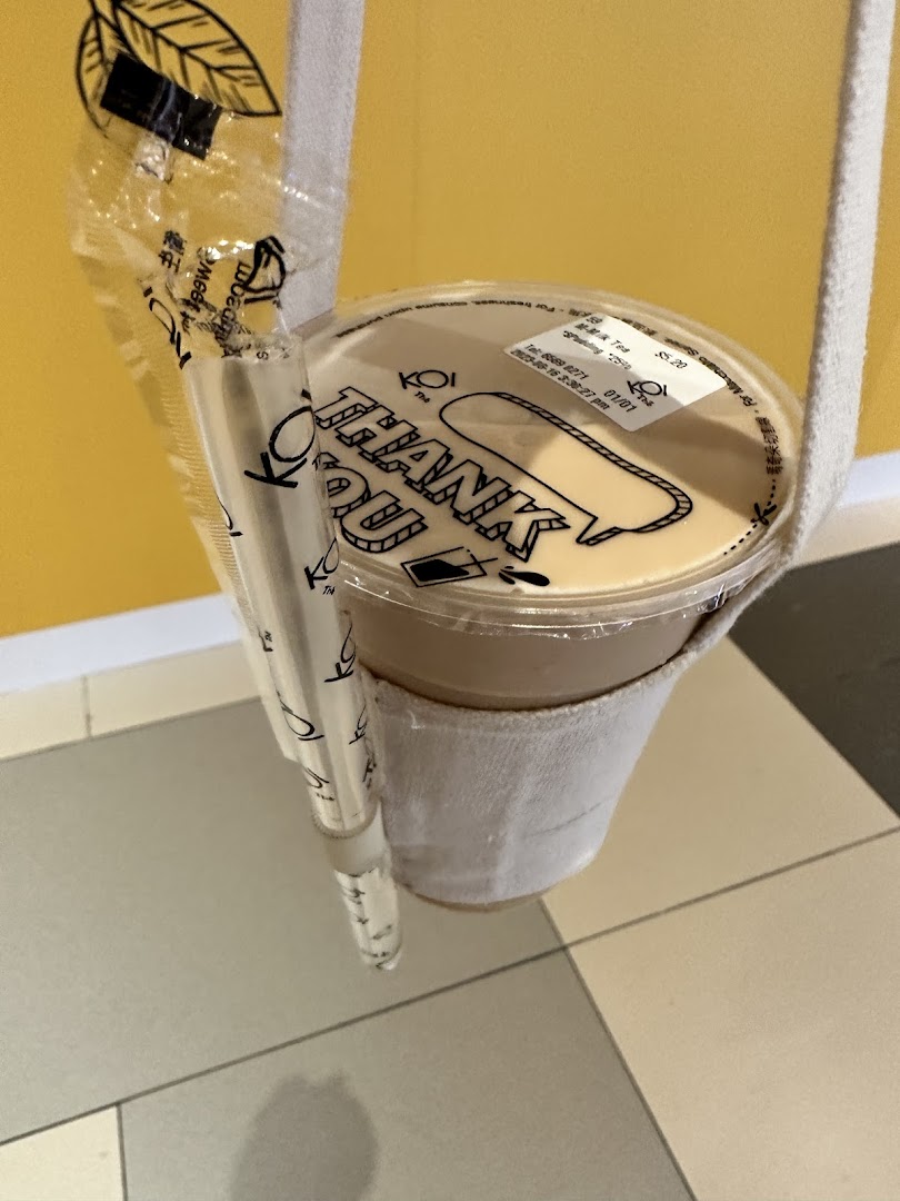 A close-up of a KOI Thé bubble tea drink with a straw in a fabric holder.