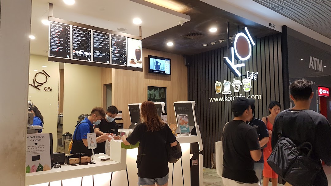 Customers order at the bustling counter of KOI Thé, featuring staff, self-service kiosks, and menu boards.