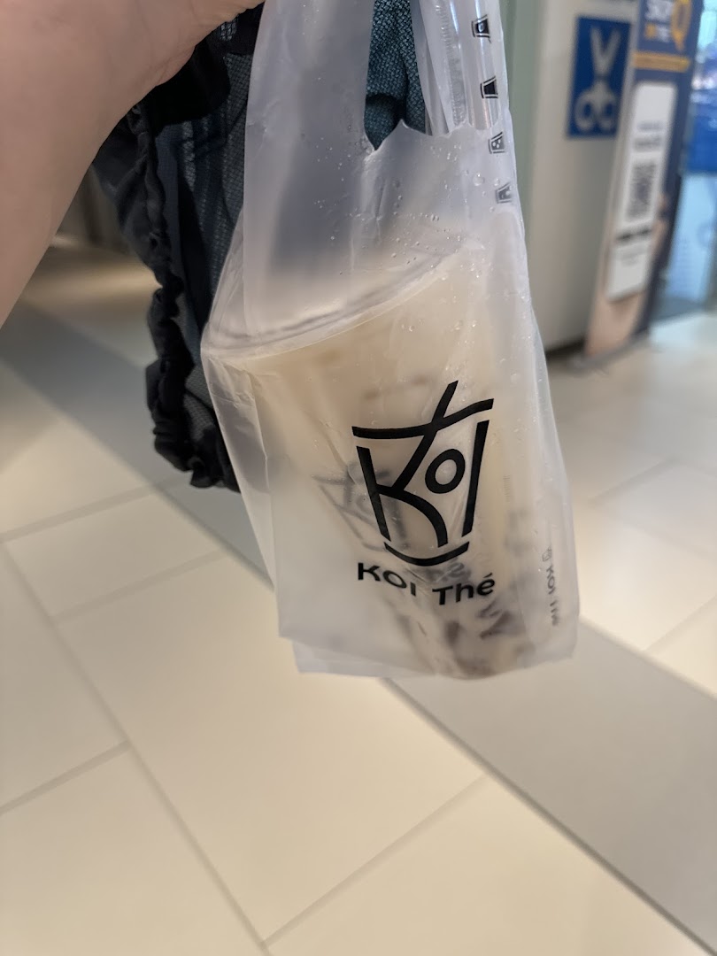 A hand holding a KOI Thé bubble tea drink in a branded plastic bag.