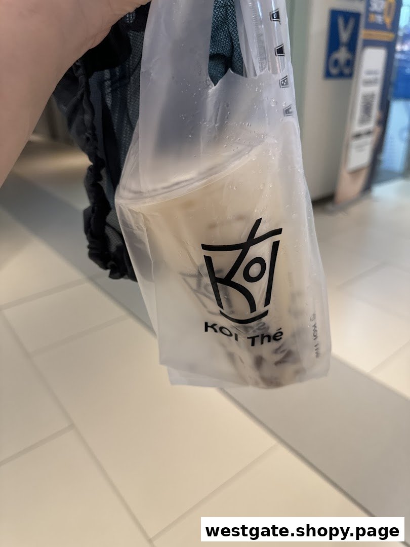 A hand holding a KOI Thé bubble tea drink in a branded plastic bag.