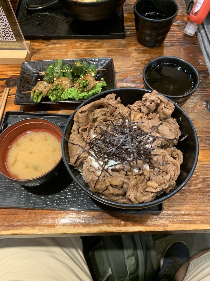 A delicious Japanese beef bowl (Gyudon) set with miso soup and grilled vegetable skewers on a wooden table.