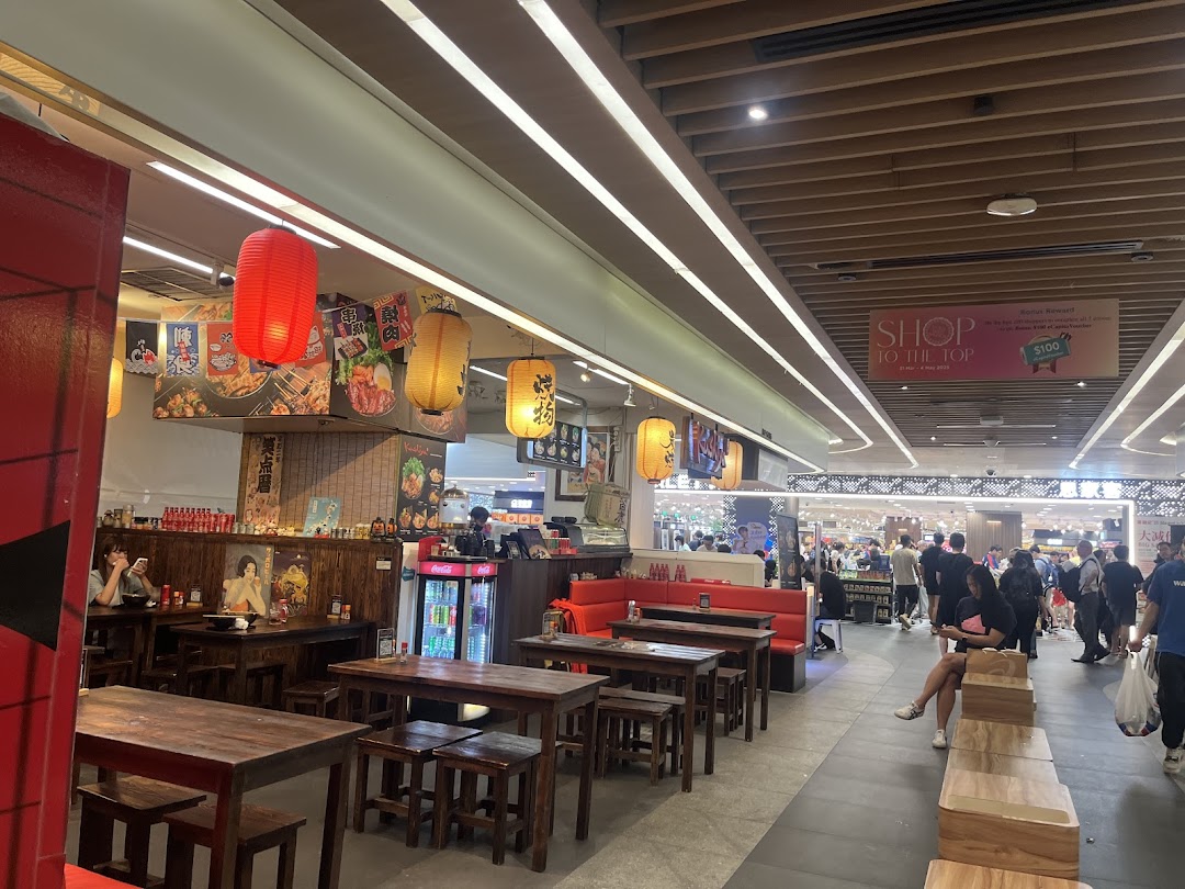 Interior view of Kushiya Japanese Grill House, featuring traditional wooden tables, red lanterns, and a lively mall backdrop.
