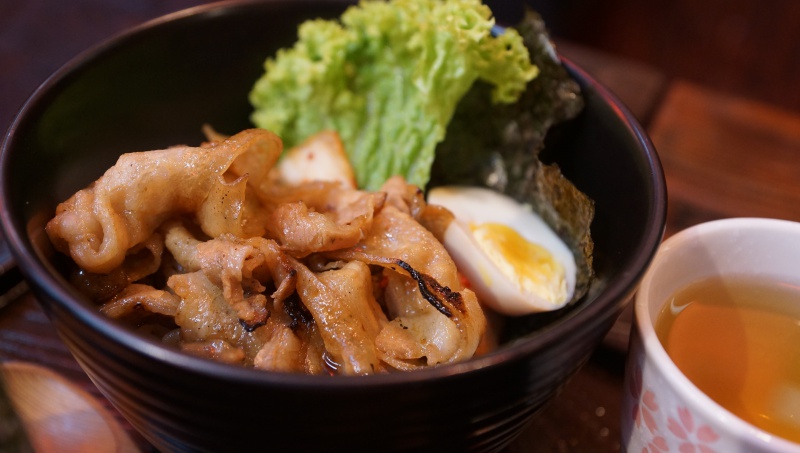 A close-up of a Japanese grilled meat bowl with lettuce, egg, seaweed, and a cup of tea.