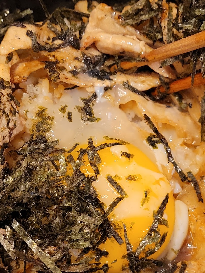A close-up of a Japanese dish featuring a raw egg yolk, shredded seaweed, and grilled meat.