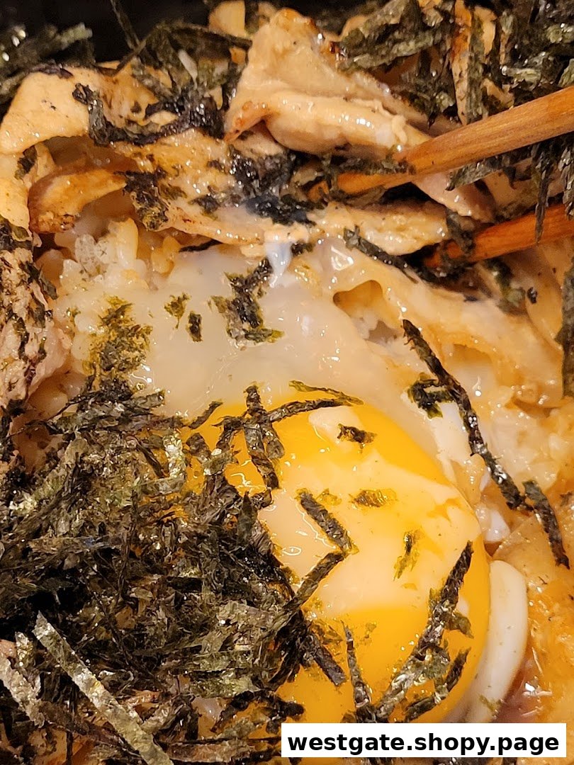 A close-up of a Japanese dish featuring a raw egg yolk, shredded seaweed, and grilled meat.