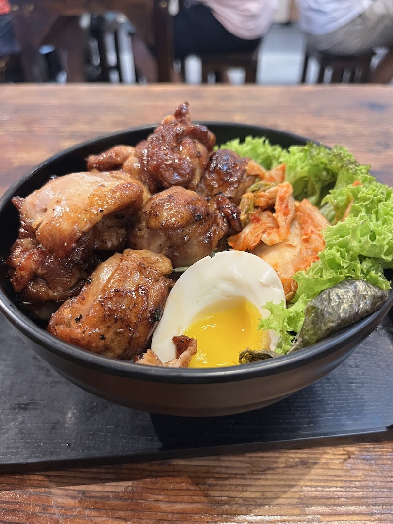 A delicious bowl featuring grilled chicken, a soft-boiled egg, kimchi, and fresh greens.