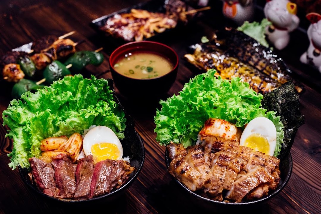 Two vibrant Japanese grill bowls with meat, egg, and fresh greens, accompanied by grilled fish and skewers.
