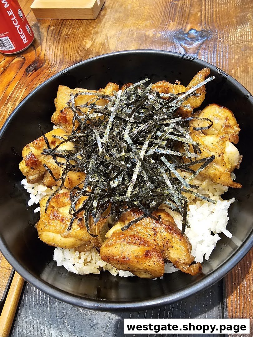 A close-up of a delicious grilled chicken rice bowl topped with shredded seaweed.