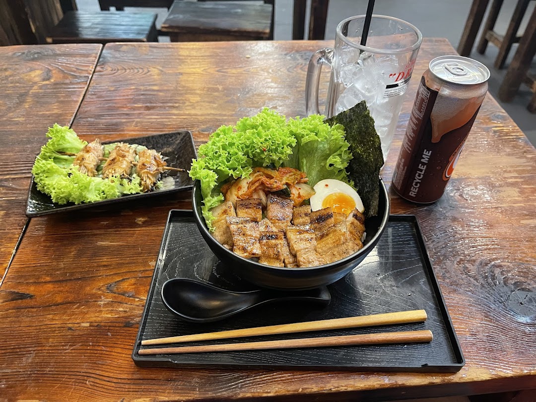 A delicious Japanese grilled pork bowl with kimchi, egg, and a side of skewers on a rustic wooden table.