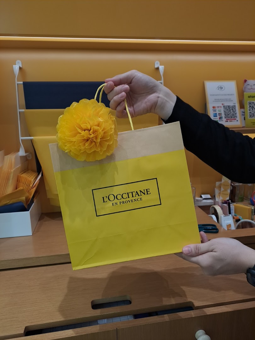 A person holds a vibrant yellow L'OCCITANE shopping bag adorned with a decorative flower.