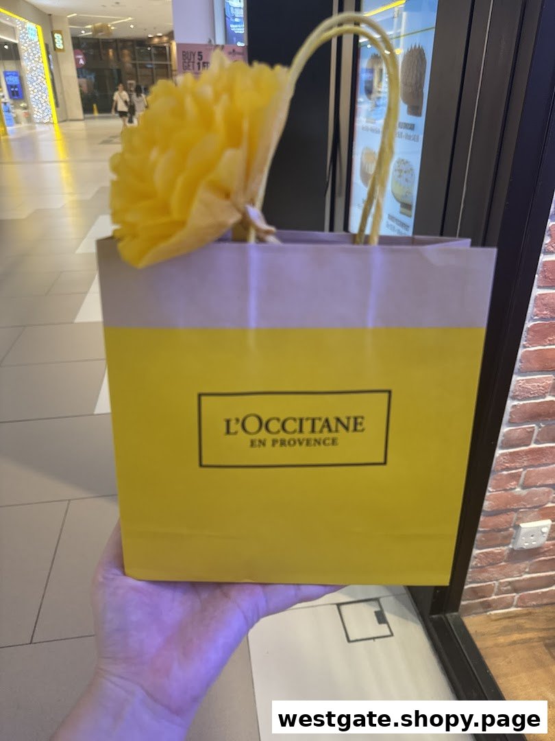 A person holds a vibrant yellow L'OCCITANE shopping bag adorned with a decorative flower inside a bustling mall.