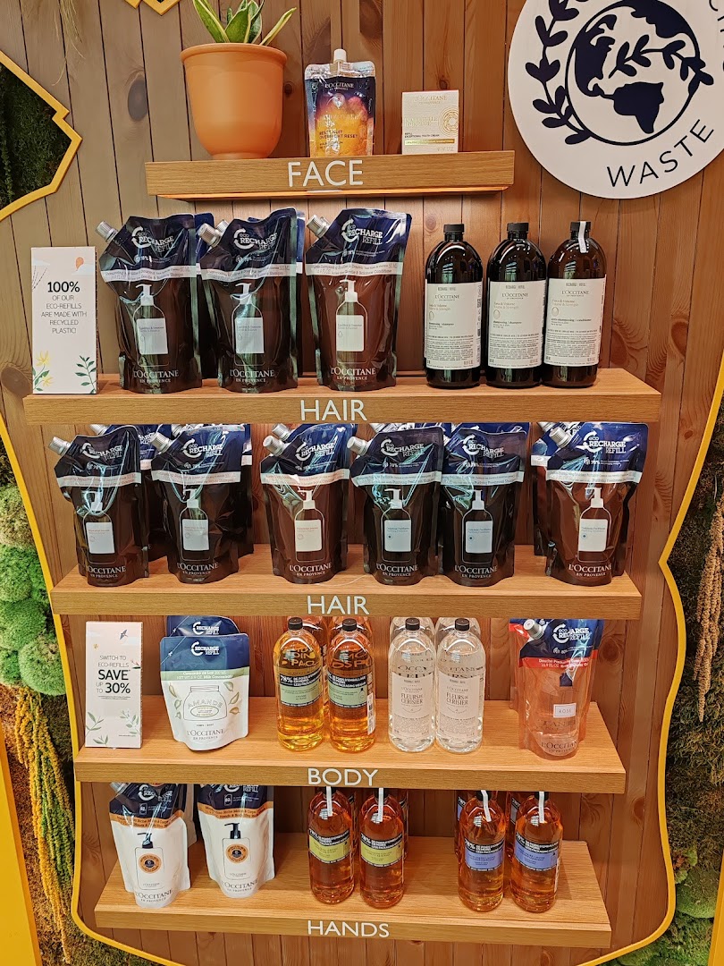 L'OCCITANE's eco-refill display featuring sustainable products for face, hair, body, and hands on wooden shelves.
