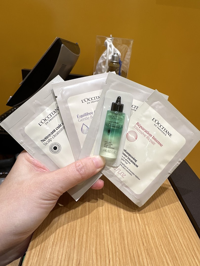 A hand holds various L'Occitane hair care product samples, including scalp cleansing and intensive repair.